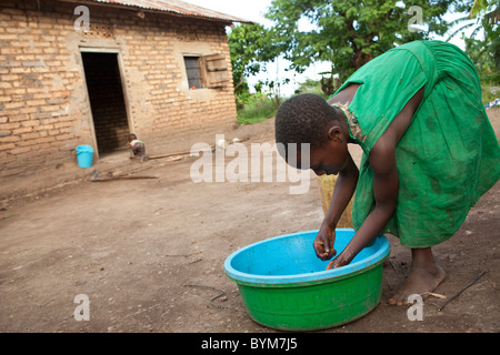 Une jeune fille se lave les mains devant sa maison dans les régions rurales de Masaka, en Ouganda, en Afrique de l'Est. Banque D'Images