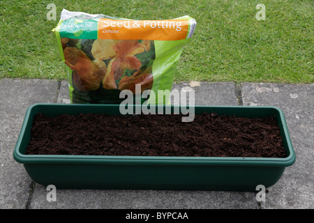 Fenêtre rectangulaire en plastique vert semoir case rempli de compost avec sac sur le patio du jardin. Banque D'Images