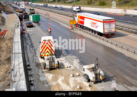 L'équipement de forage de béton dans les trous formant barrière pour l'écrasement de la route au cours de projet d'élargissement autoroute M25 Banque D'Images