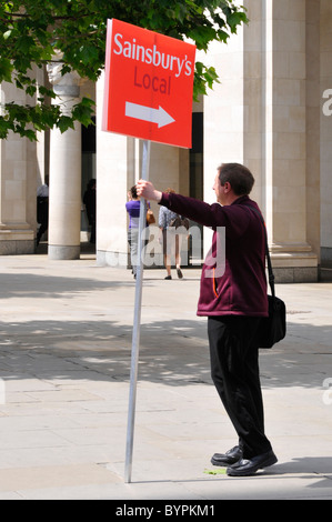 Man holding placard panneau indiquant à l'emplacement d'un nouveau supermarché Sainsburys Local food store récemment ouvert dans la ville de London England UK Banque D'Images