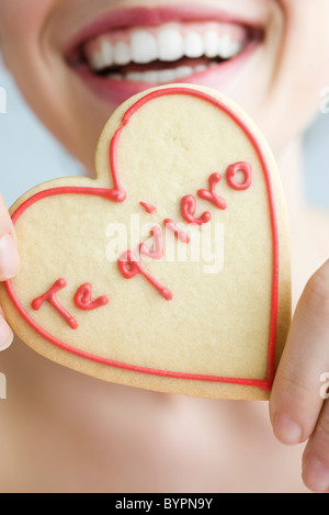 Woman holding up heart-shaped cookie, smiling, portrait Banque D'Images