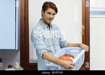 Portrait de hot young man looking at camera avec panier de vêtements. De forme horizontale, side view Banque D'Images