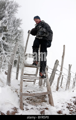 En hiver, un randonneur randonnées un stile dans la réserve naturelle des volcans d'Auvergne (France). Randonneur franchissant un échalier. Banque D'Images