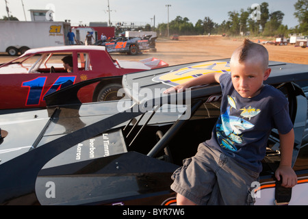 USA, au Mississippi, Gulfport, jeune garçon avec coupe de cheveux mohawk se trouve sur race car dans les fosses au sud du Mississippi Speedway Banque D'Images