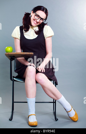 Coy geeky school girl full length smiling at her desk Banque D'Images