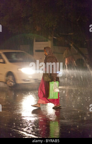 L'Inde, l'Uttar Pradesh, Agra dame crossing road dans de fortes pluies de mousson Banque D'Images