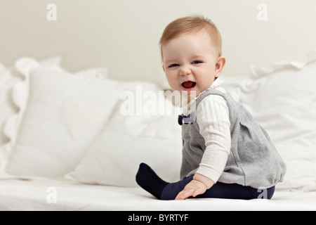 Portrait de 6 mois femme enfant jouant sur bed and smiling at camera. Vue de côté, de forme horizontale, pleine longueur, copy space Banque D'Images