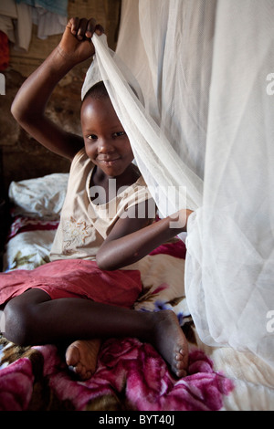 Un enfant tire un moustiquaire ovaer son lit avant de dormir à Kampala, Ouganda Banque D'Images