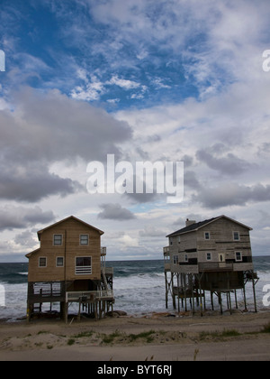 Tôt le matin, ciel dramatique accents l'érosion des plages et des vagues sous les maisons condamnées sur l'Océan Atlantique Banque D'Images