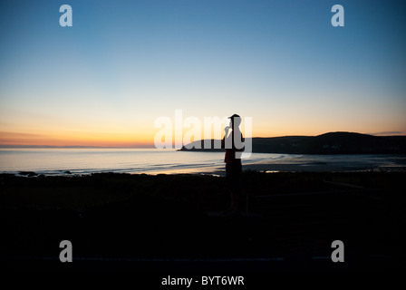 Un homme regarde le soleil se coucher sur la baie de Croyde Devon, UK Banque D'Images