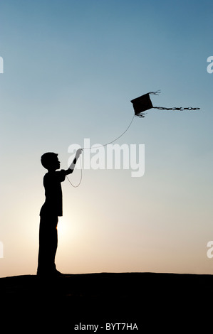 Jeune Indien garçon s'amusant voler un cerf-volant de papier fait main dans la campagne indienne. Silhouette Banque D'Images