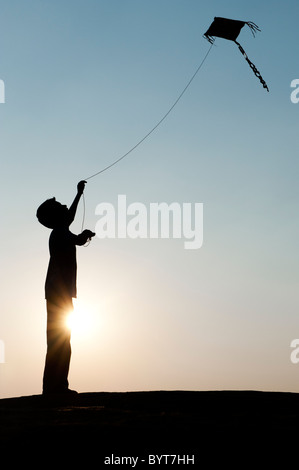 Jeune Indien garçon s'amusant voler un cerf-volant de papier fait main dans la campagne indienne. Silhouette Banque D'Images