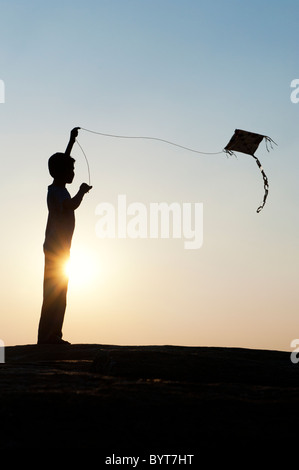 Jeune Indien garçon s'amusant voler un cerf-volant de papier fait main dans la campagne indienne. Silhouette Banque D'Images