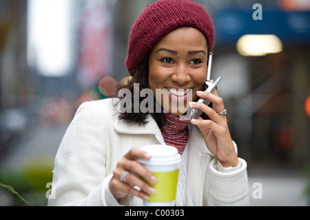 Une femme d'affaires moderne dans la ville parle sur son téléphone cellulaire tout en profitant d'une tasse de café. Banque D'Images