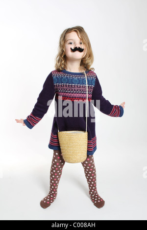 Un long shot of a little white caucasian girl looking at camera avec une fausse moustache noire, les bras et les doigts Banque D'Images