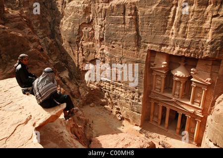 Bédouins assis sur le dessus d'une falaise à la recherche vers le bas pour le Trésor (El khazneh), Petra, Jordanie. Banque D'Images