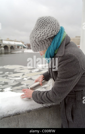 La jeune fille dans une gelée blanche foulard bleu, un chapeau gris et un manteau verse de un thermos dans une tasse de thé chaud sur Pushkinsky quay Banque D'Images