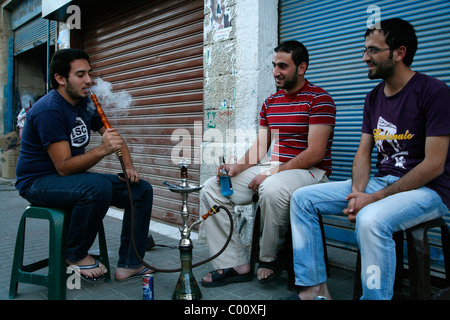 Les jeunes hommes fumeurs narguilé (pipe à eau) dans une rue de Madaba, Jordanie. Banque D'Images