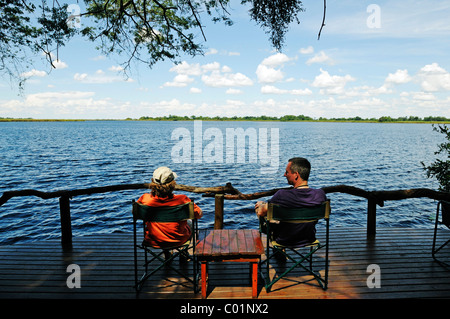 Les touristes assis sur la terrasse d'un lodge sur le Guma Lagoon, Okavango Delta, Botswana, Africa Banque D'Images