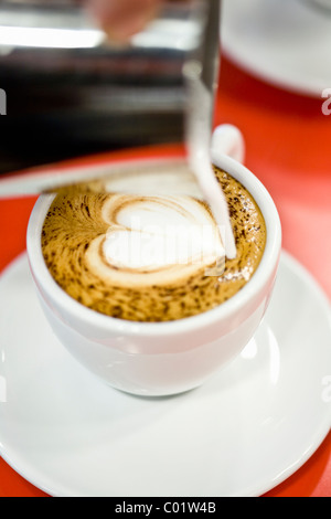 Le lait chaud est versé dans une tasse pour prendre un cappuccino Banque D'Images