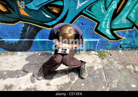 Dix-année-vieux garçon jouant avec sa Nintendo en face d'un mur de graffiti, Germany, Europe Banque D'Images