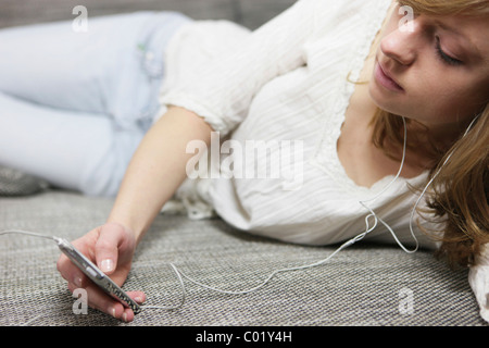 Jeune femme couchée sur un canapé avec un lecteur MP3, écouter de la musique avec des écouteurs Banque D'Images