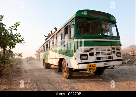 Indian bus voyageant le long d'une route de campagne avec des gens assis sur le toit. L'Andhra Pradesh, Inde Banque D'Images
