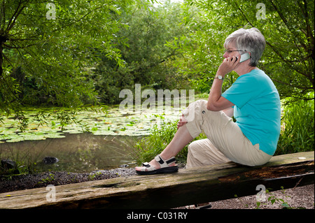 Femme assise sur un banc à une forêt, lac de parler sur son téléphone portable Banque D'Images