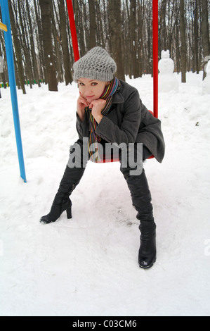 La jeune fille est assise sur une balançoire pour les enfants dans le parc en hiver, Moscou, Russie Banque D'Images