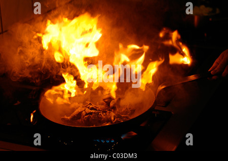 Flamme explosif dans une poêle avec une viande sur une cuisinière à gaz avec graisse qui est trop chaude Banque D'Images