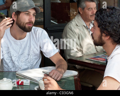 Beau jeune homme mexicain de baseball cap fumeurs avec un ami au coin salon extérieur sidewalk cafe dans quartier rom de la ville de Mexico Banque D'Images