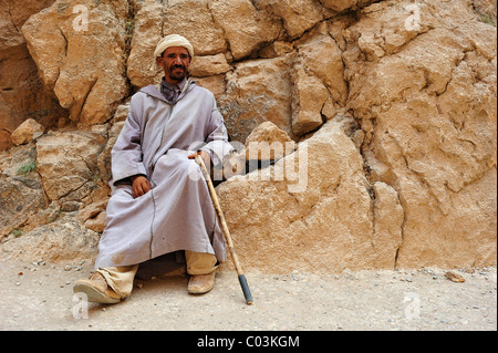 Personnes âgées Le Berbère homme portant une djellaba et un turban appuyé contre une paroi de rochers, Gorges de Todra, le Maroc, l'Afrique Banque D'Images