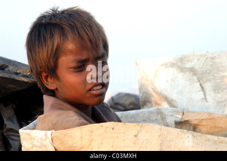 Un jeune garçon qui est un enfant travailleur est assis dans un grand sac à déchets toxiques et polluée à un vidage de la corbeille au Cambodge. Banque D'Images