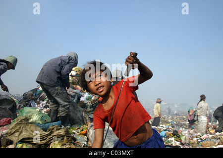 Un jeune garçon qui est un enfant travailleur est la collecte de plastique avec une corne à un dangereux et pollué dépotoir au Cambodge. Banque D'Images