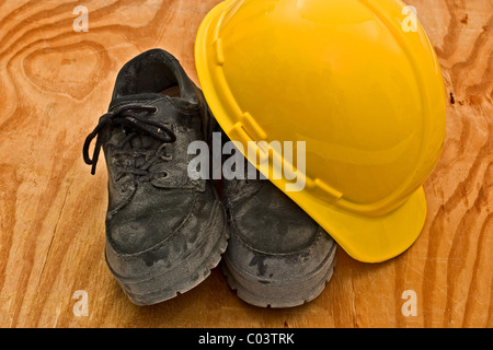 Casque jaune sur le dessus d'une paire de chaussures de travail sale épais Banque D'Images