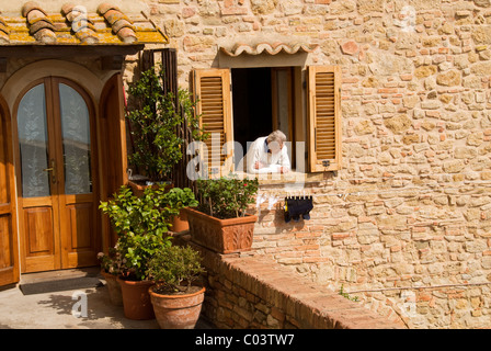 Vieille Femme italienne en regardant par la fenêtre de sa maison, Volterra, Toscane, Italie Banque D'Images