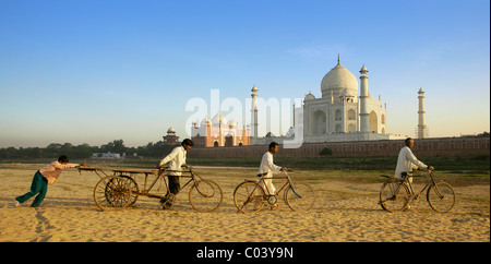 L'Inde, l'Uttar Pradesh, Agra, poussant les hommes et les garçons dans l'ensemble des vélos à sec de la rivière Yamuna avec Taj Mahal au-delà Banque D'Images