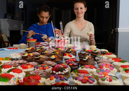Deux adolescentes decorating cupcakes fait maison sur une table pour une grande partie Banque D'Images