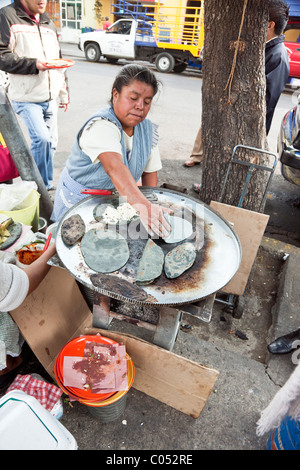 Genial occupé dans la cuisine mexicaine impeccable tablier Vichy bleu travaillant sur son grill de tacos de maïs bleu sur trottoir quartier rom de Banque D'Images