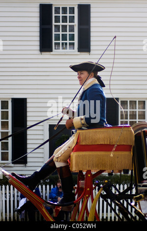 Un cocher avec un fouet sur chariot roulant siège par un accueil dans la ville historique de Colonial Williamsburg, VA. Banque D'Images