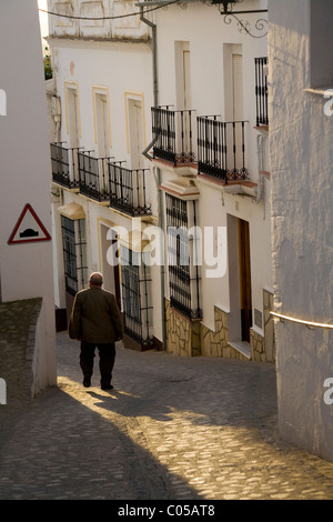 Homme marche dans les rues pavées traditionnelles espagnoles / Rue / Route, et bâtiments au crépuscule dans le village blanc de Zahara, Espagne Banque D'Images