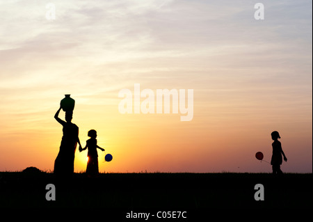 Mère indienne portant de l'eau pot avec des enfants et des ballons dans la campagne indienne. Silhouette Banque D'Images