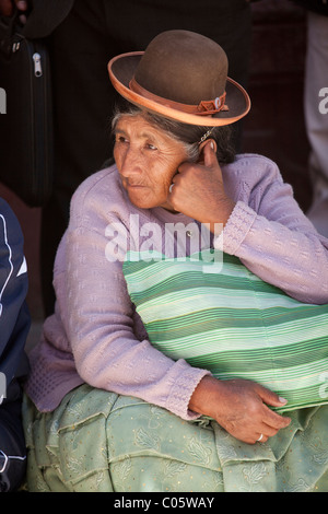 Une femme péruvienne dans un style traditionnel chapeau melon est assis sur le côté de la route et regarde la parade Semaine Puo Banque D'Images