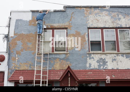 Une nouvelle couche de peinture sur un bâtiment ancien. Un peintre d'une grande échelle applique une nouvelle couche de peinture blanche sur un mal de stuc en flocons Banque D'Images