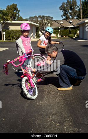 Papa règle le son de roues de formation 5 ans fille vélo comme elle apprend à monter avec sa soeur. Parution du modèle Banque D'Images