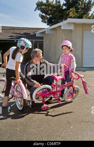 Papa et grande sœur ajuster les roues d'entraînement de ses cinq ans, fille de location comme elle apprend à conduire en Californie. Banque D'Images