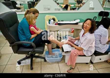 Une Vietnamienne technicien effectue une pédicure pour une femme comme elle tient sa fille dans un salon de la Californie du Sud. Banque D'Images