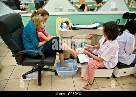 Une Vietnamienne technicien effectue une pédicure pour une femme comme elle tient sa fille dans un salon de la Californie du Sud. Banque D'Images