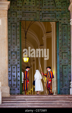 Nun promenades par entrée de la Cité du Vatican entre les protecteurs de l'armée suisse en uniforme traditionnel, Rome, Latium, Italie Banque D'Images