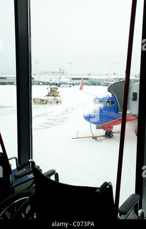 Fauteuil roulant vide assis devant une fenêtre donnant sur l'enlèvement de la neige dans un aéroport fermé dans la Nouvelle Angleterre. Banque D'Images